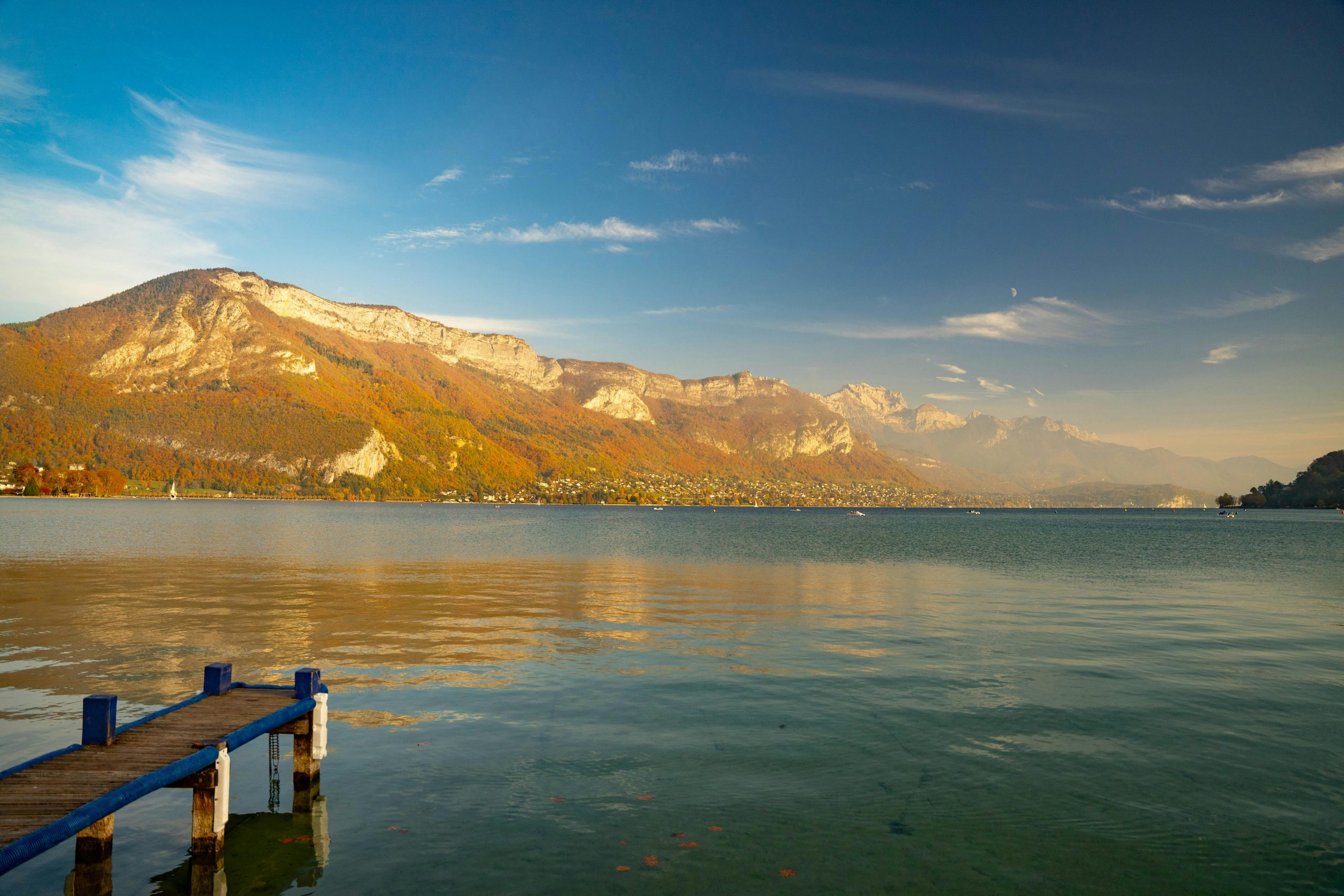 Paysage d'automne serein du lac d'Annecy avec les montagnes environnantes et un ciel clair.