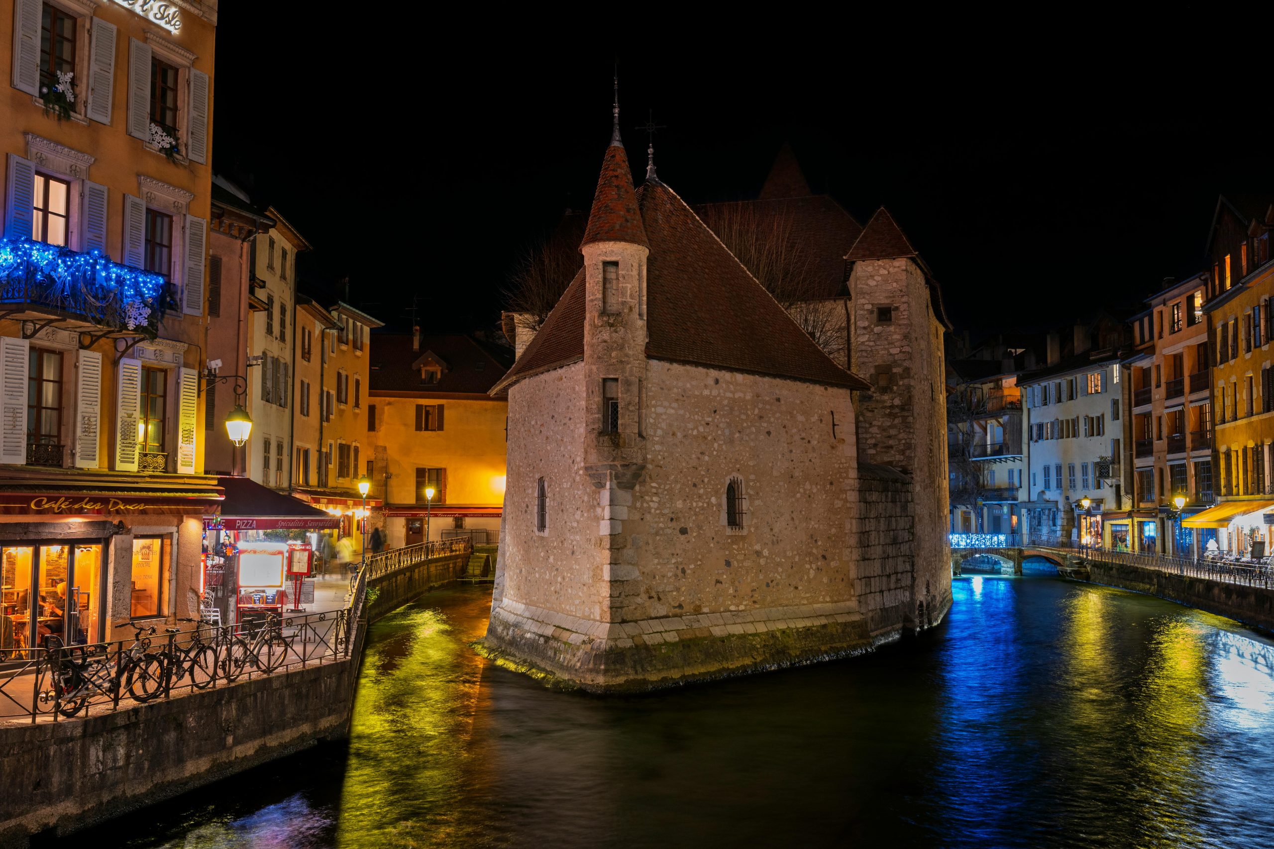 Scène nocturne captivante de l'emblématique château d'Annecy entouré de canaux illuminés.