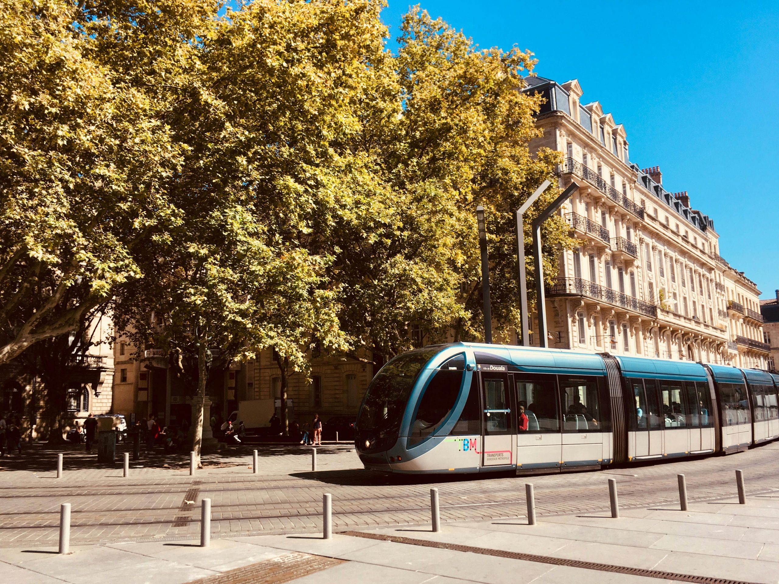 Un tramway élégant traverse les rues ensoleillées de Bordeaux, entouré d'une architecture historique et d'une végétation luxuriante.
