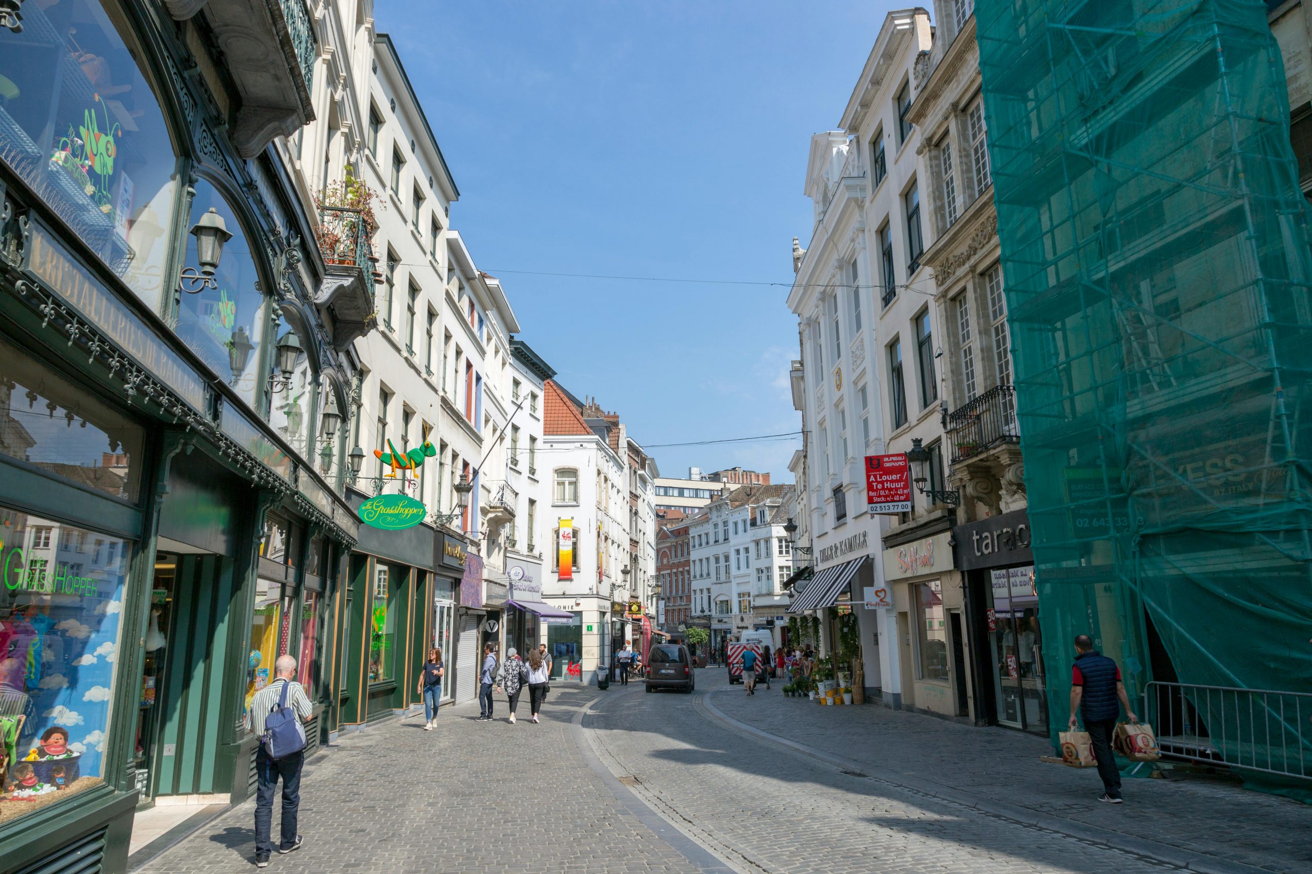 Journée ensoleillée dans une rue a Bruxelles animée avec des boutiques, des piétons et une architecture classique.