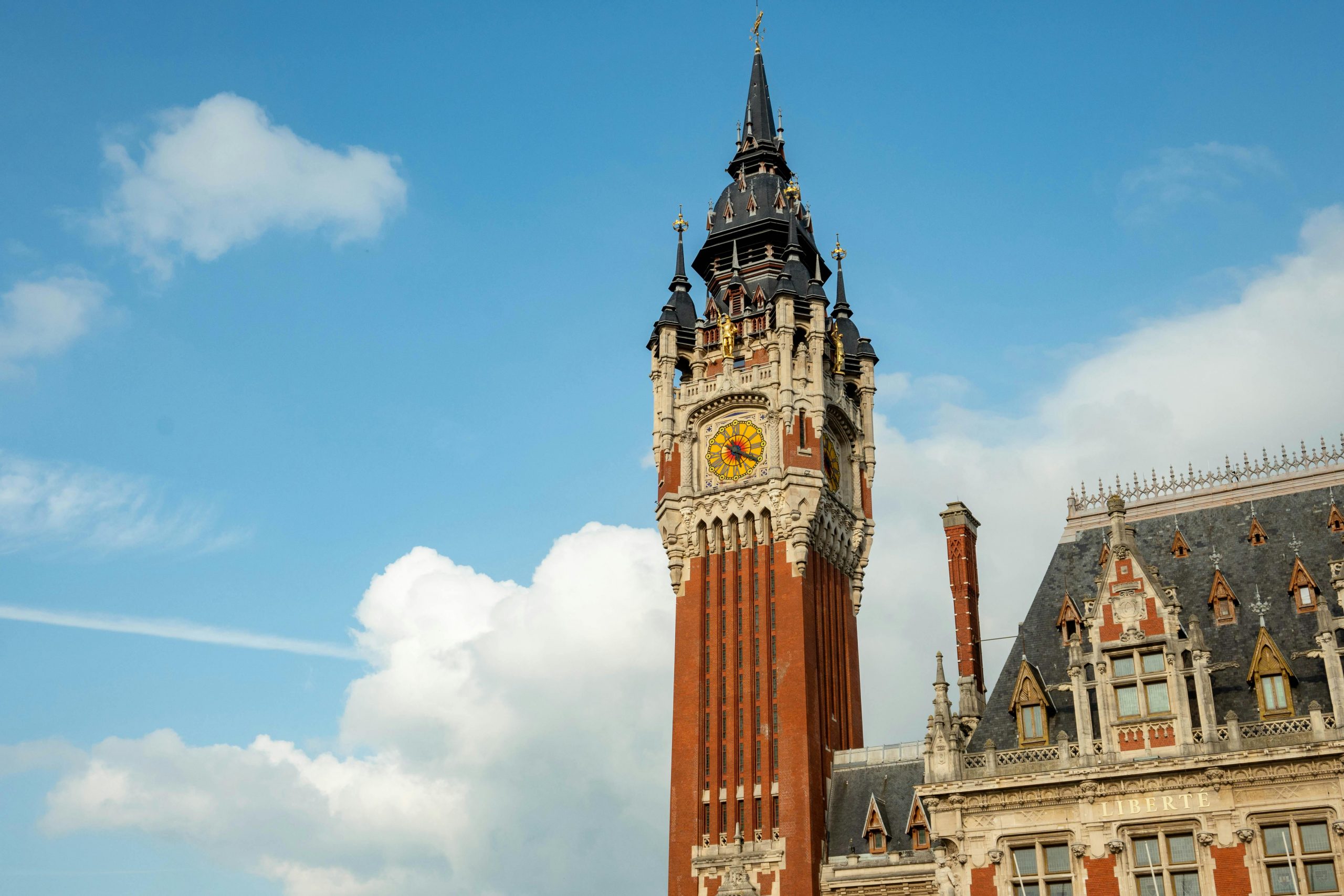 Vue imprenable sur l'emblématique beffroi de Calais contre un ciel bleu, mettant en valeur l'architecture néogothique.
