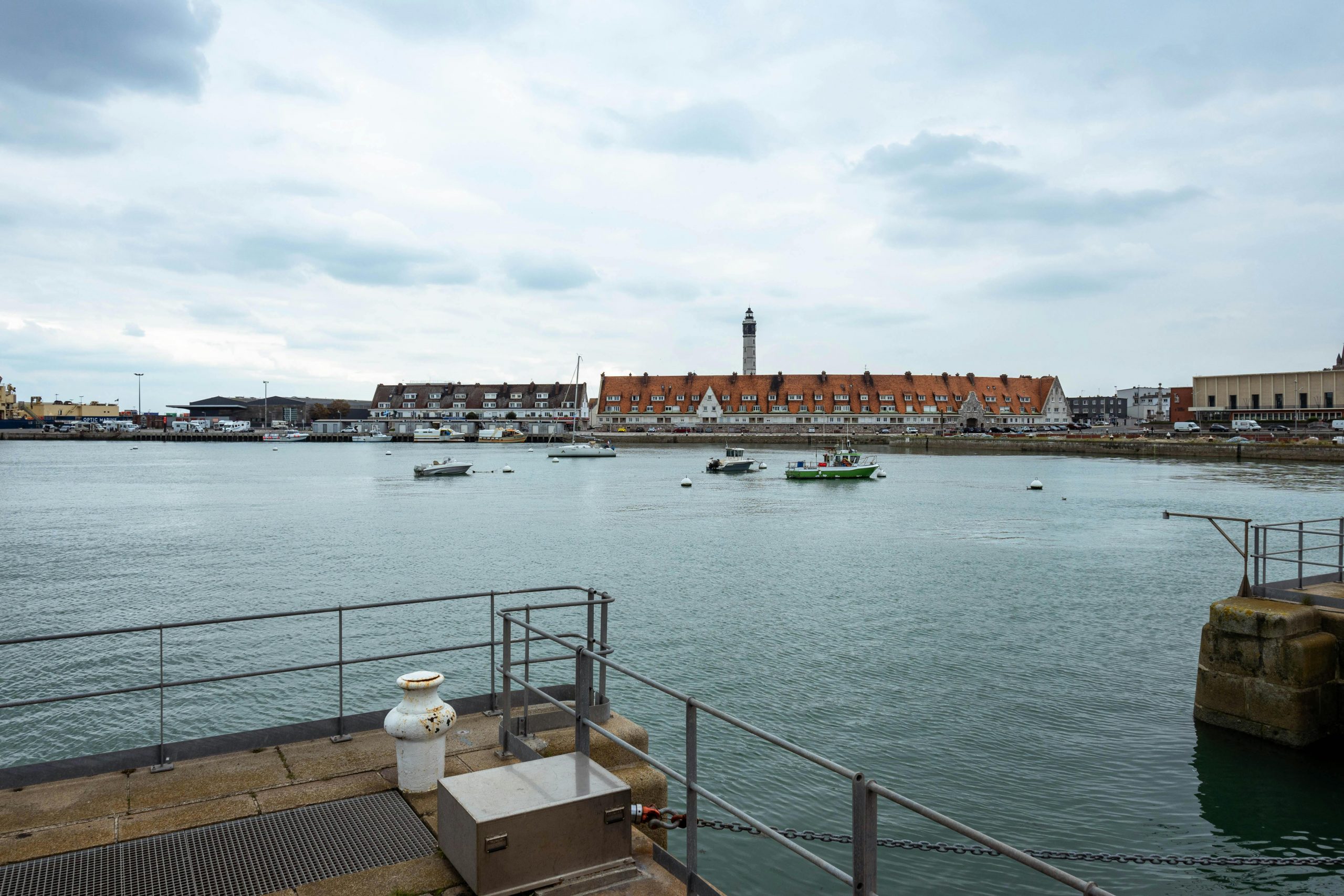 Vue panoramique du port de Calais, avec un phare et des bateaux sous un ciel nuageux.