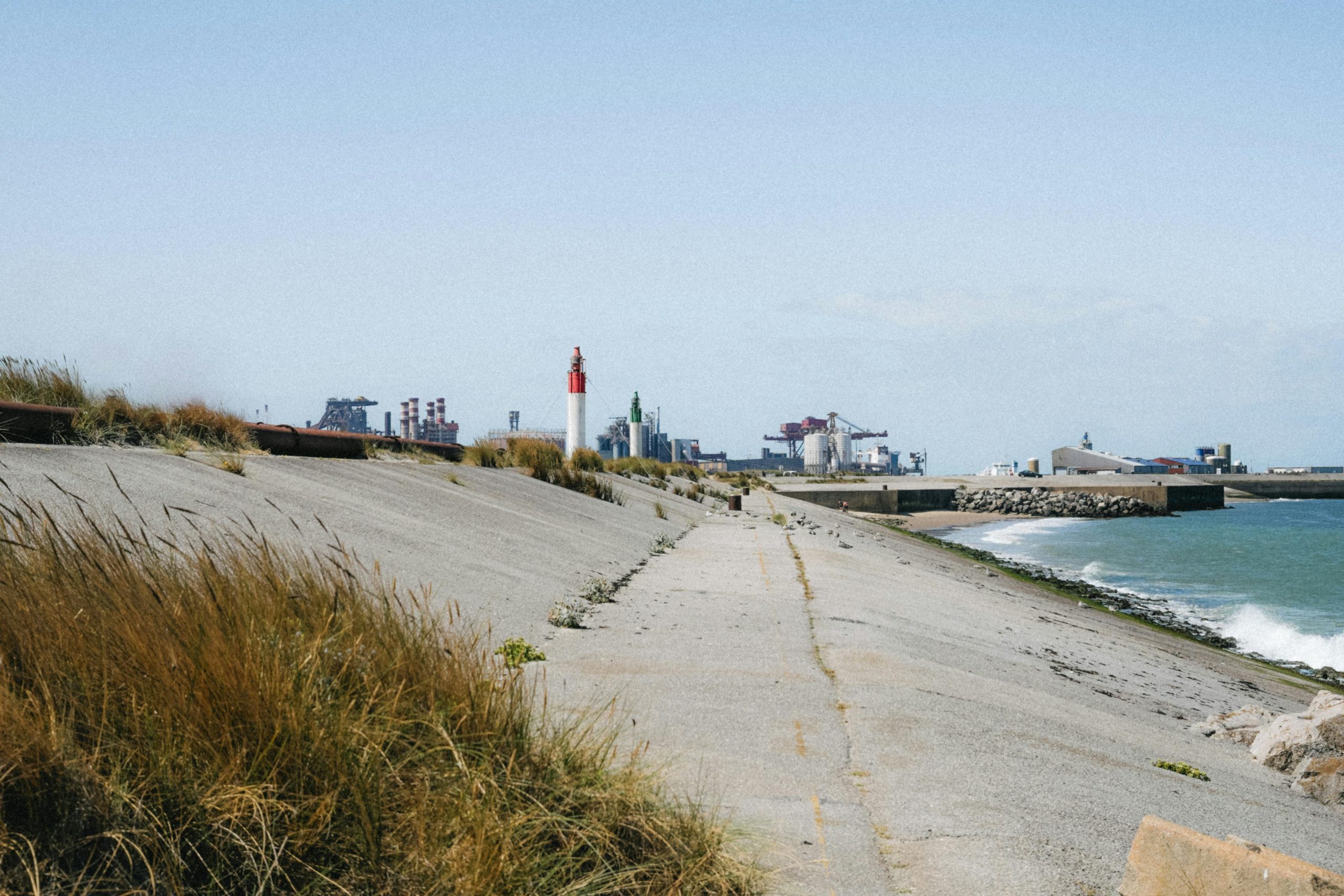 Vue panoramique du littoral de Dunkerque avec au loin des bâtiments industriels et un phare.