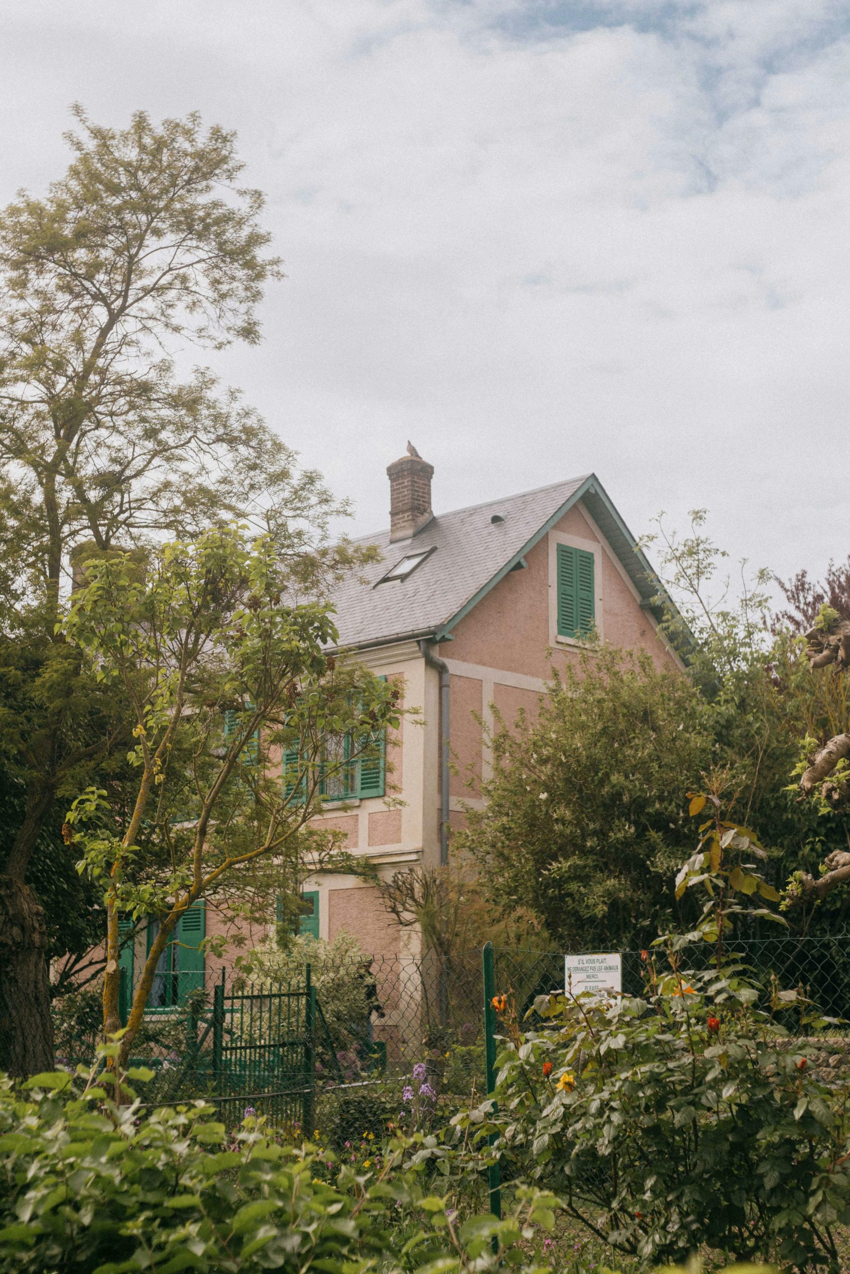 Une maison rose pittoresque entourée de verdure luxuriante et de fleurs par une journée nuageuse.