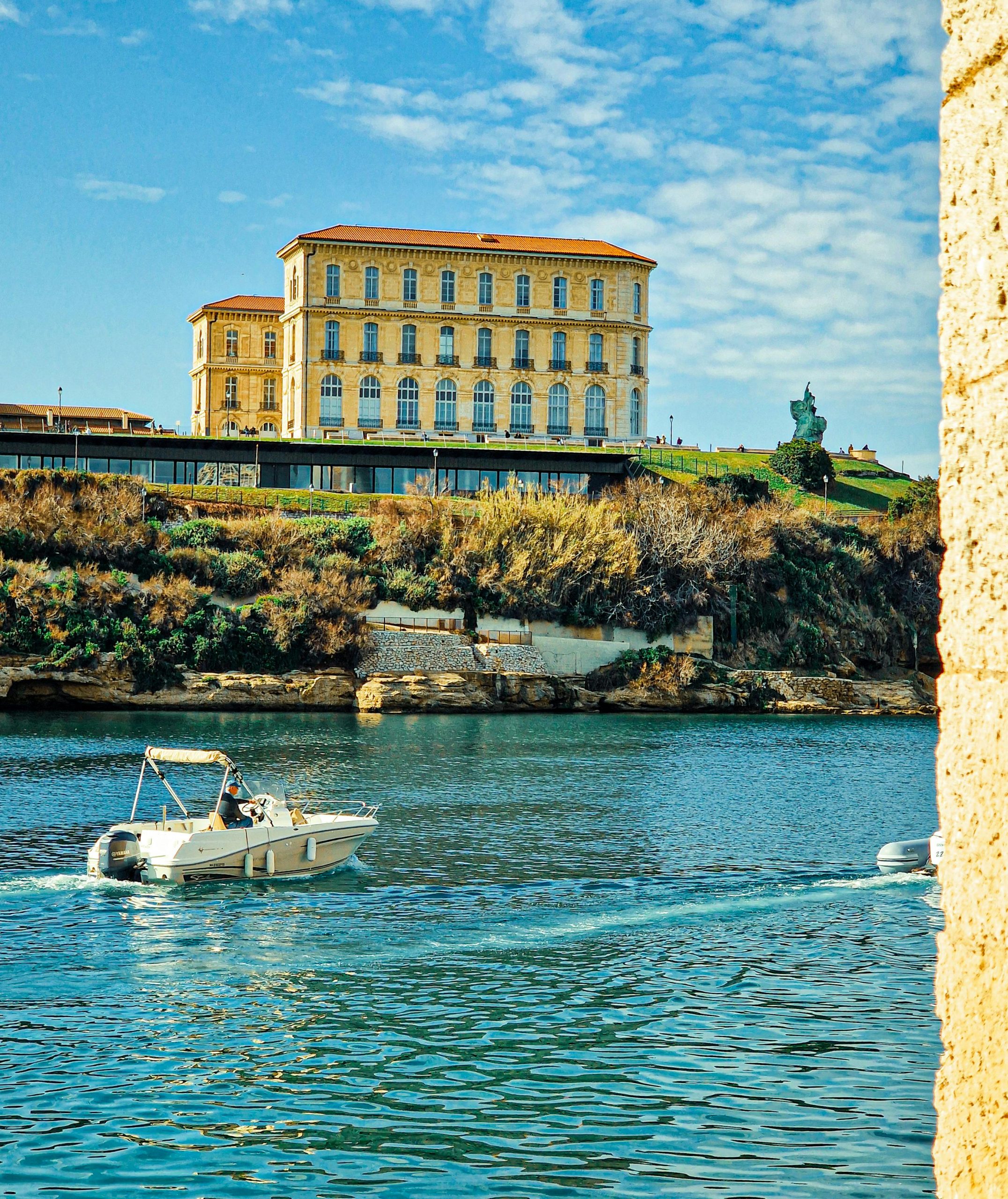 Un bateau navigue devant le Palais du Pharo, monument historique, sous un ciel d'un bleu éclatant à Marseille, en France.