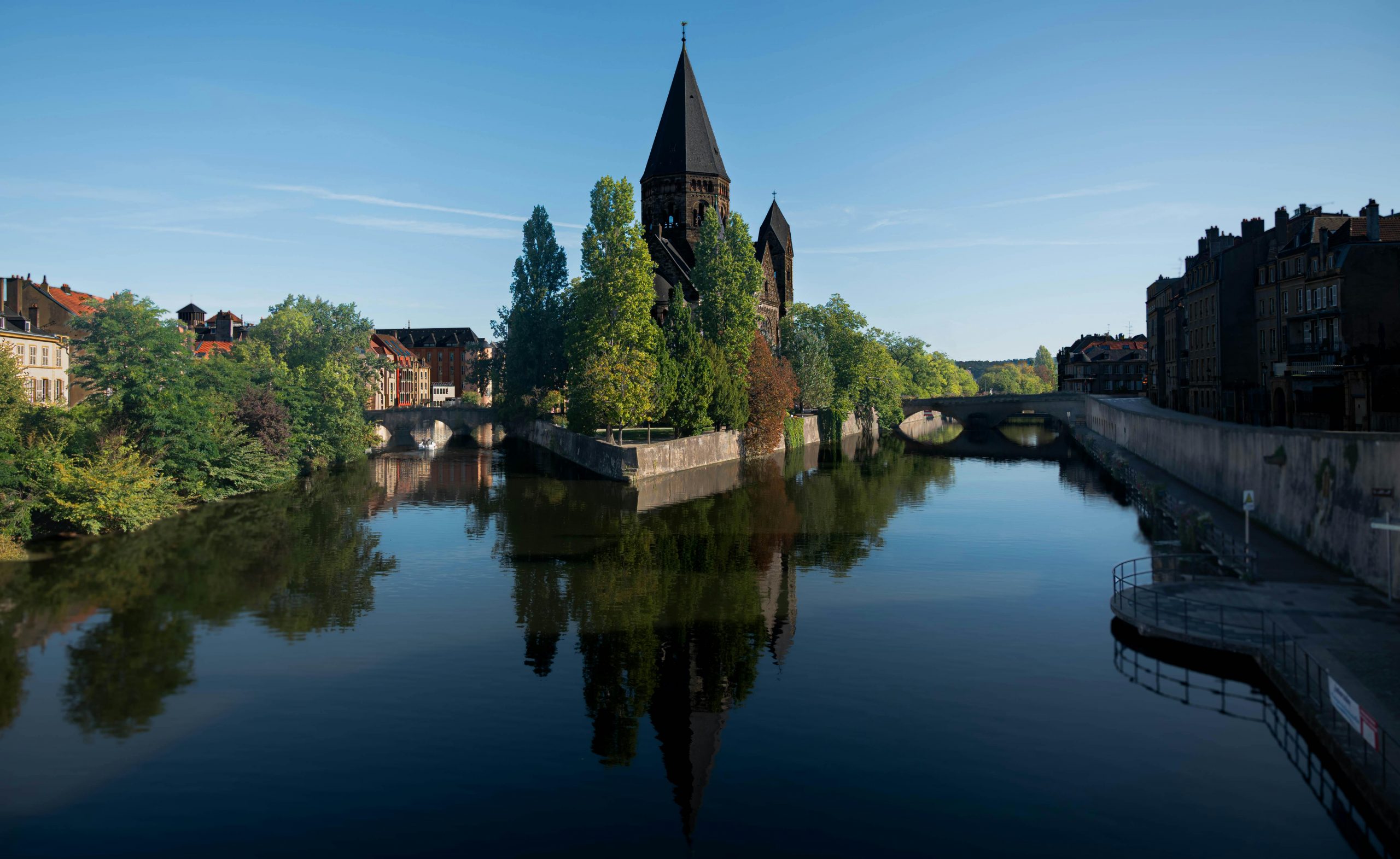 Vue pittoresque d'une église historique se reflétant dans une rivière calme sous un ciel bleu limpide.