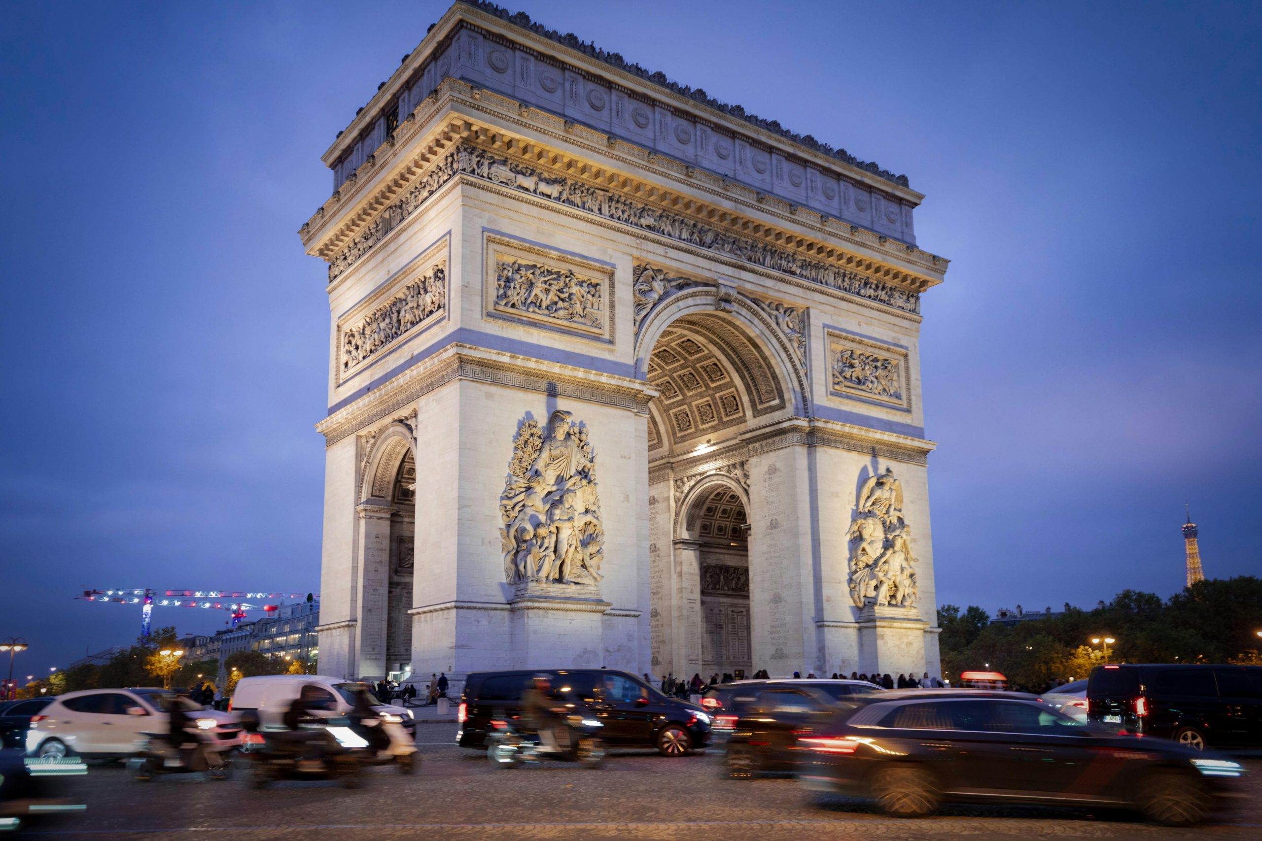 L'emblématique Arc de Triomphe sous un ciel bleu du soir avec un trafic animé à Paris.