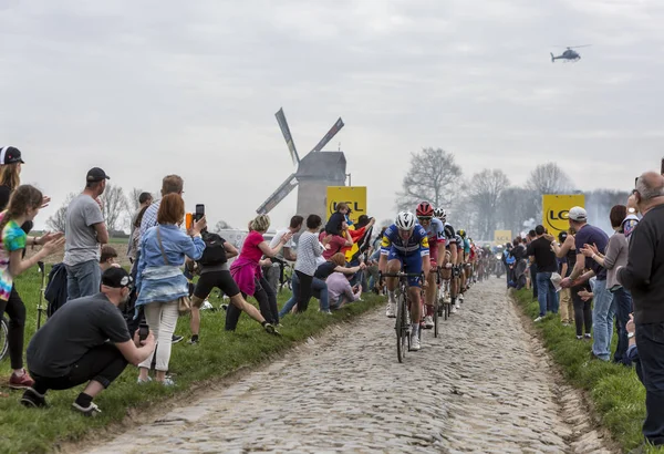 Templeuve, France - 08 avril 2018 : Le peloton sur la route pavée de Templeuve devant le traditionnel moulin à vent du Vertain lors de Paris-Roubaix 2018.