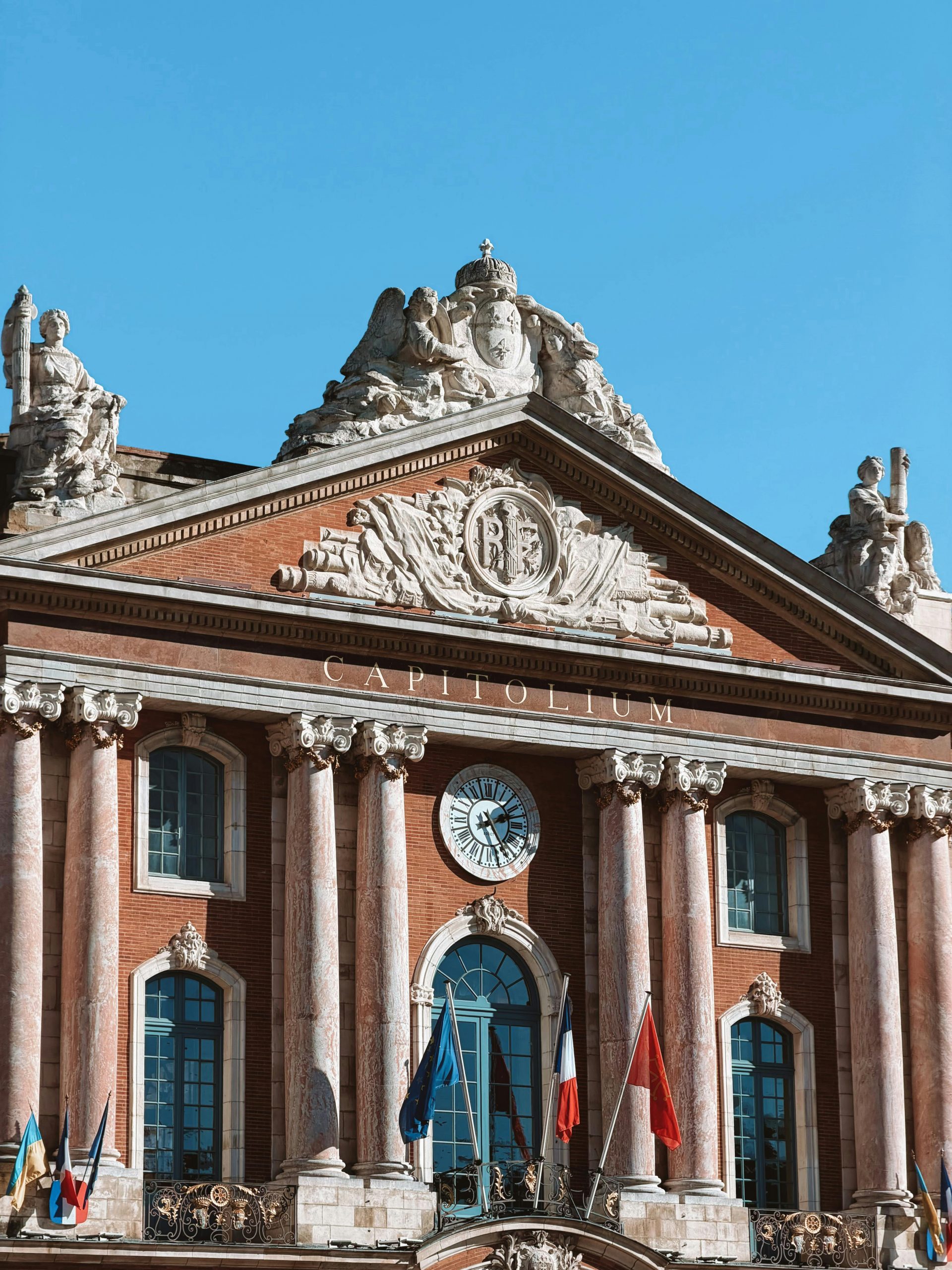 Gros plan sur la façade du Capitole à Toulouse, ornée de sculptures classiques et de drapeaux.